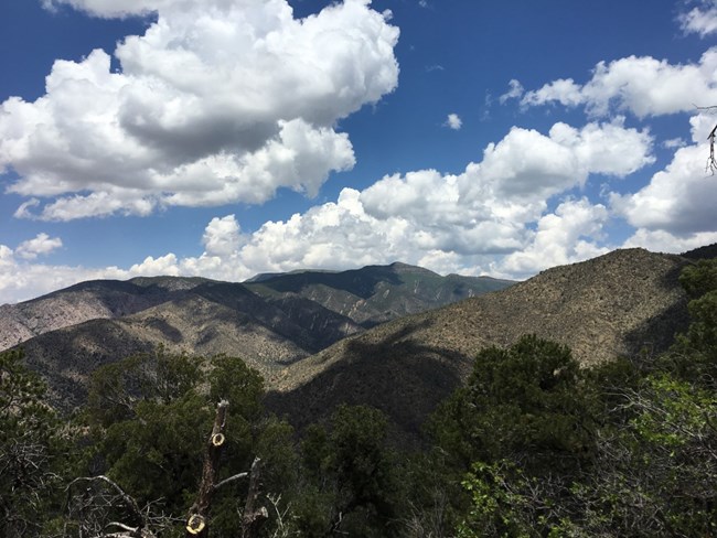 A vegetated mountain range with clouds overhead.