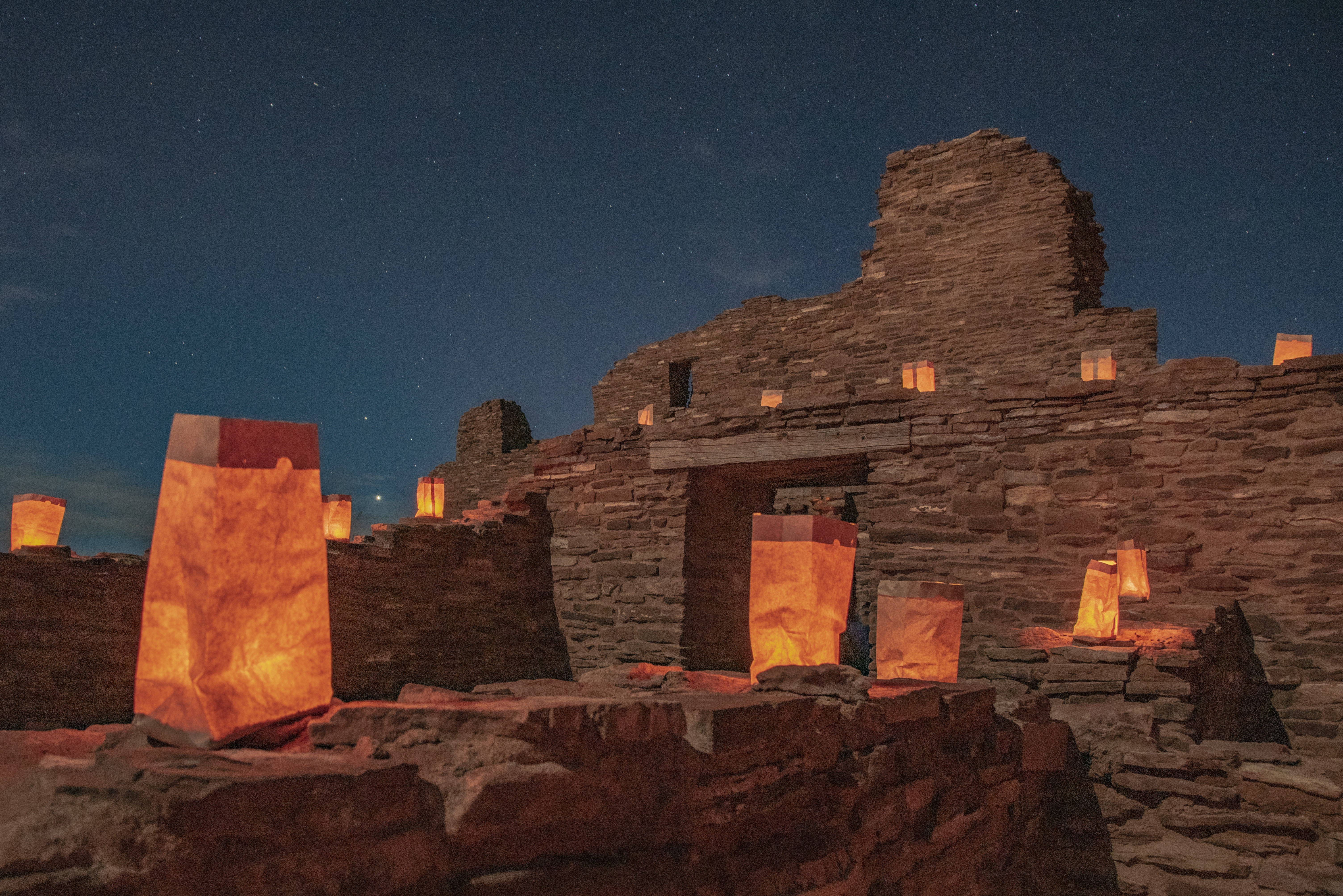 Lit luminarias with red sandstone ruins in the background.