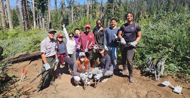 A group of volunteers with tools pose on a trail.