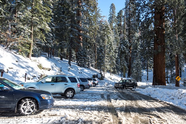 A car pulls into a snowy parking lot full of cars.