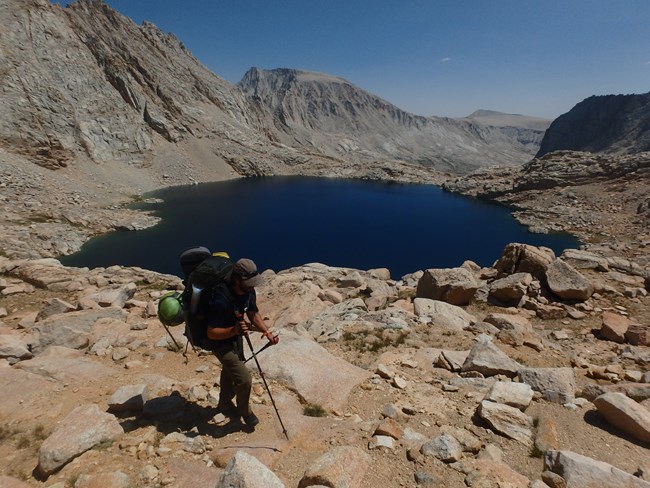Backpacker hikes up rocky pass from mountain lake below.