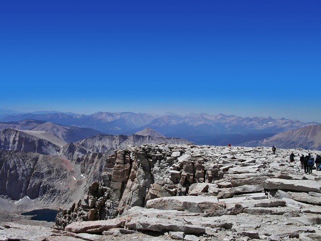 Scattered hikers walk across large granite slabs at the top of Mount Whitney