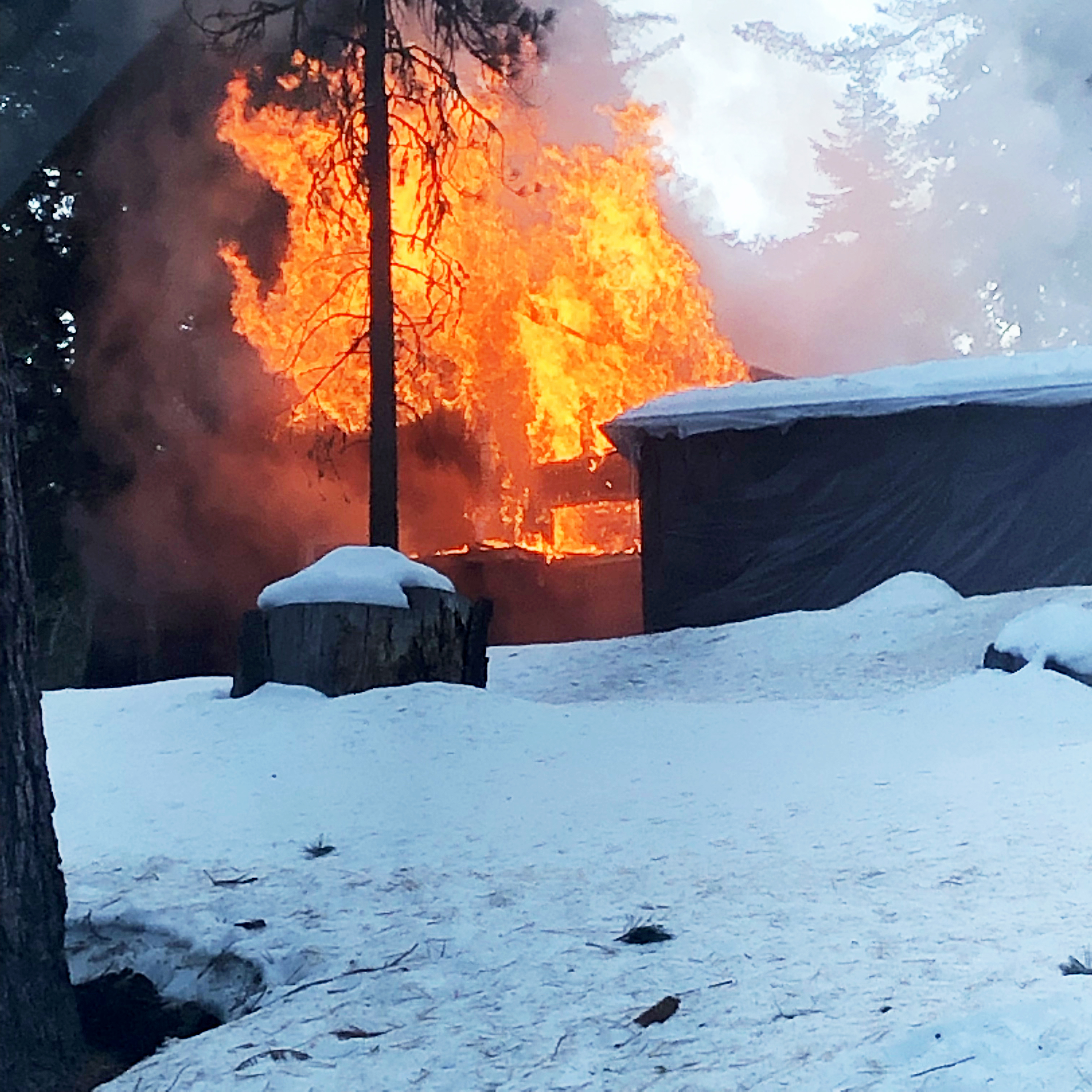 A non-residential building is fully engulfed in flames. A brown building obstructs the view completely. Snow is in the foreground.