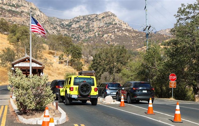 A group of cars lined up in front of a park entrance station in the foothills.