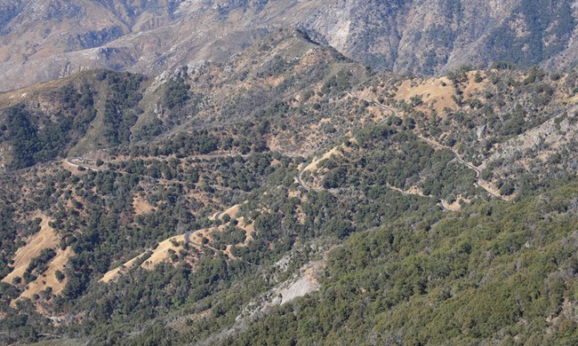 A winding road through brown hills with multiple cars.