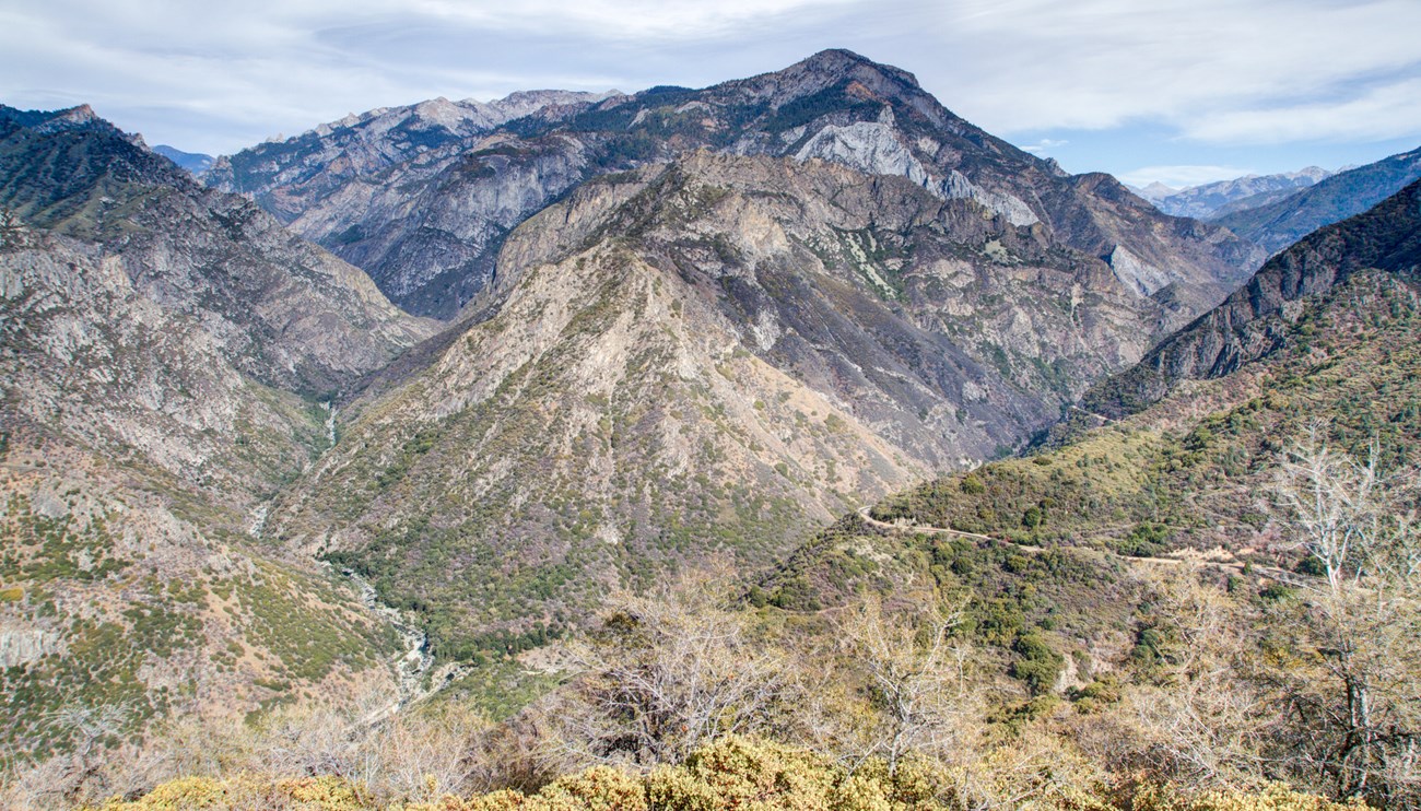 A deep canyon with a winding road leading towards a river.