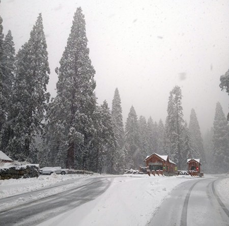 A brown log entrance station blanketed in snow, with flurries in the air.