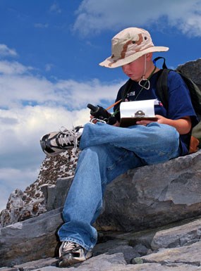 A young visitor sits on the rocks to study his GPS Unit while EarthCaching.