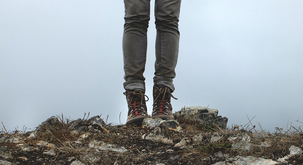 A close up of hiking boots standing on rocks in front of a cloudy viewpoint