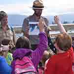 Park Ranger holding picture in front of young students with mountains in the background.