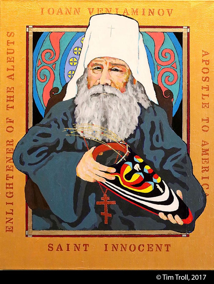 Stylized painting of an elderly white man with long gray beard wearing a tall white orthodox priest's hat, blue robes and red Russian Orthodox cross, holding a brightly painted visor. Gold paint frames the image.