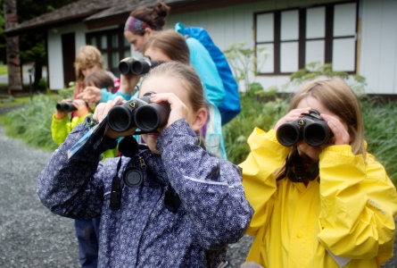 A group of kids in rain jackets looking through binoculars.