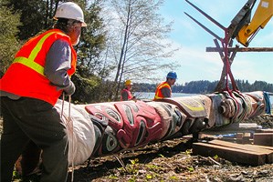 Three people positioning a totem pole with the help of construction equipment.