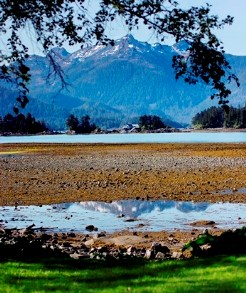 Tall, forested mountains in the background are reflected in tidal pools in the foreground.