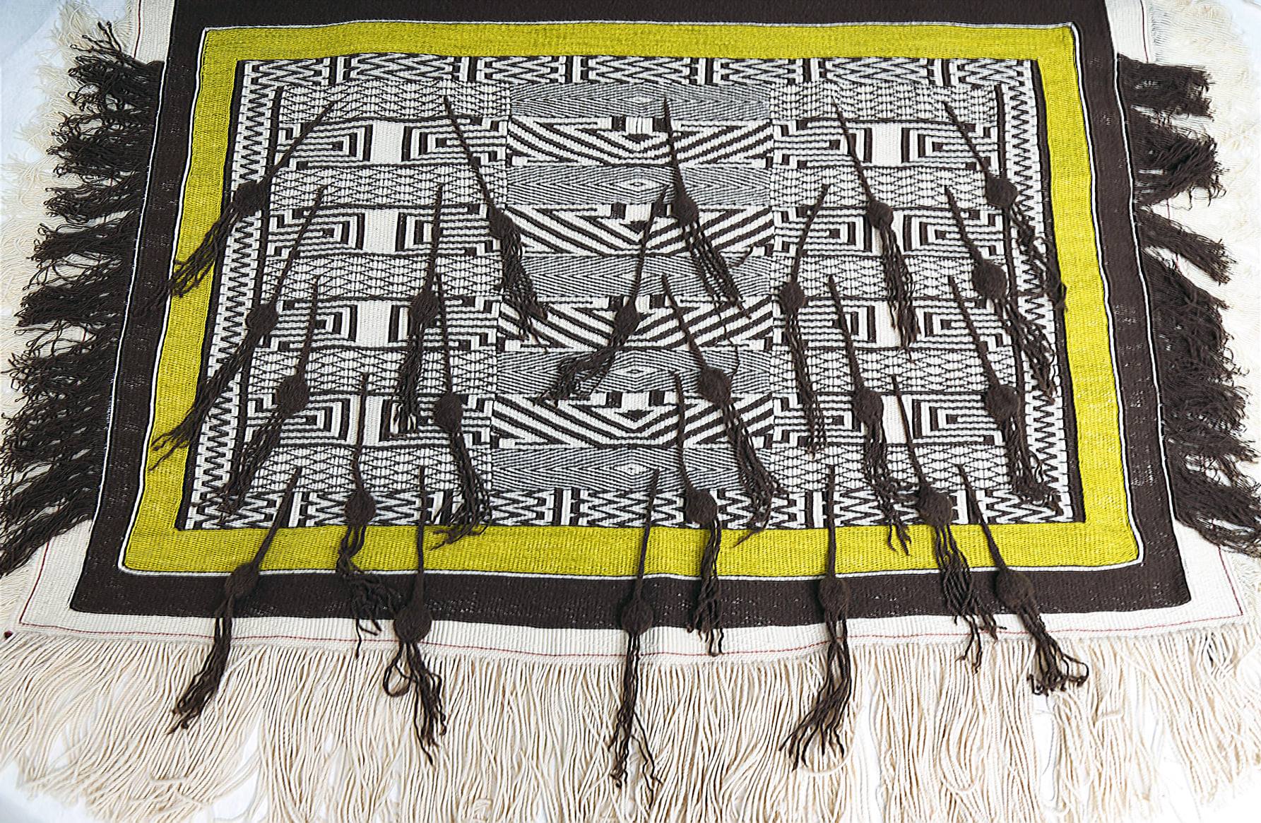 A woven textile in brown, white, and yellow with white and brown tassels and fringe