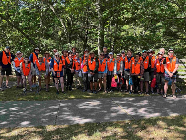 Large group of people with neon vests, equipped with trashbags and gloves to clean up.