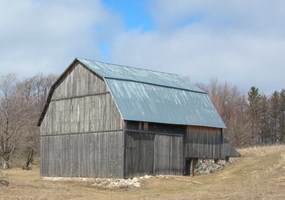 A wood barn with a metal roof in a field of brown grass.