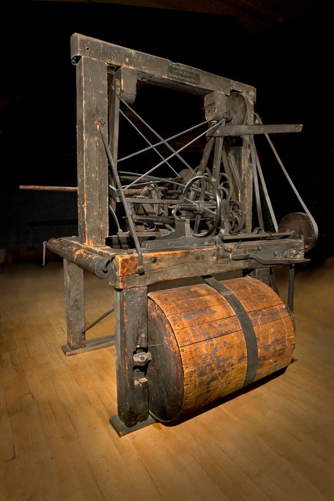 The Blanchard Lathe. The machine sits on a wood floor with a black background.