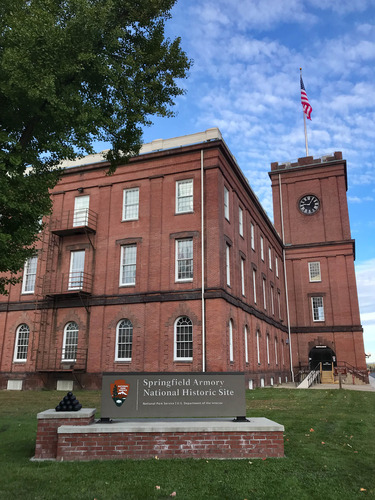 A sign saying "Springfield Armory National Historic Site" stands before a large brick arsenal and clocktower.