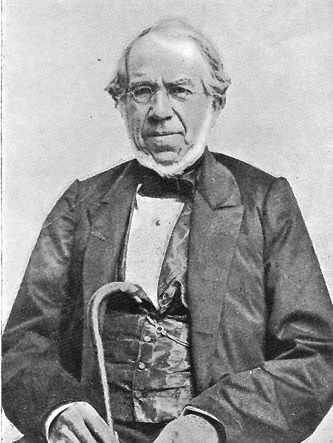 A black and white portrait of Thomas Blanchard. He is wearing a suit and holding a cane.