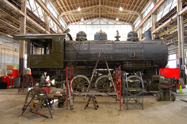 Partially disassembled locomotive in large shop building with high ceiling