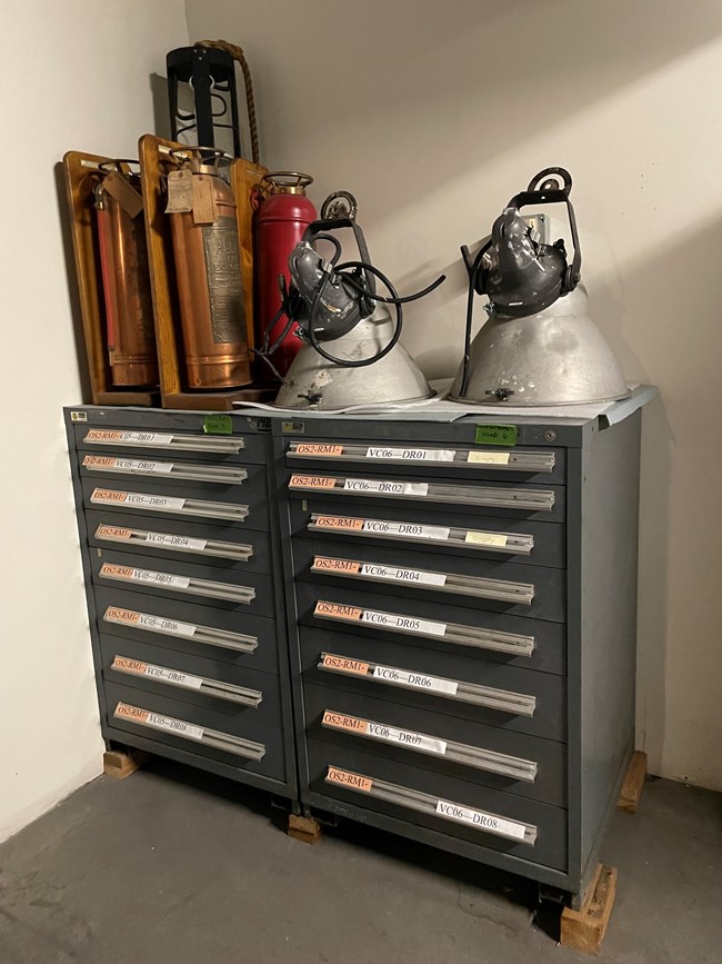 Archival storage cabinet with historic light fixtures and fire extinguishers on top of it.