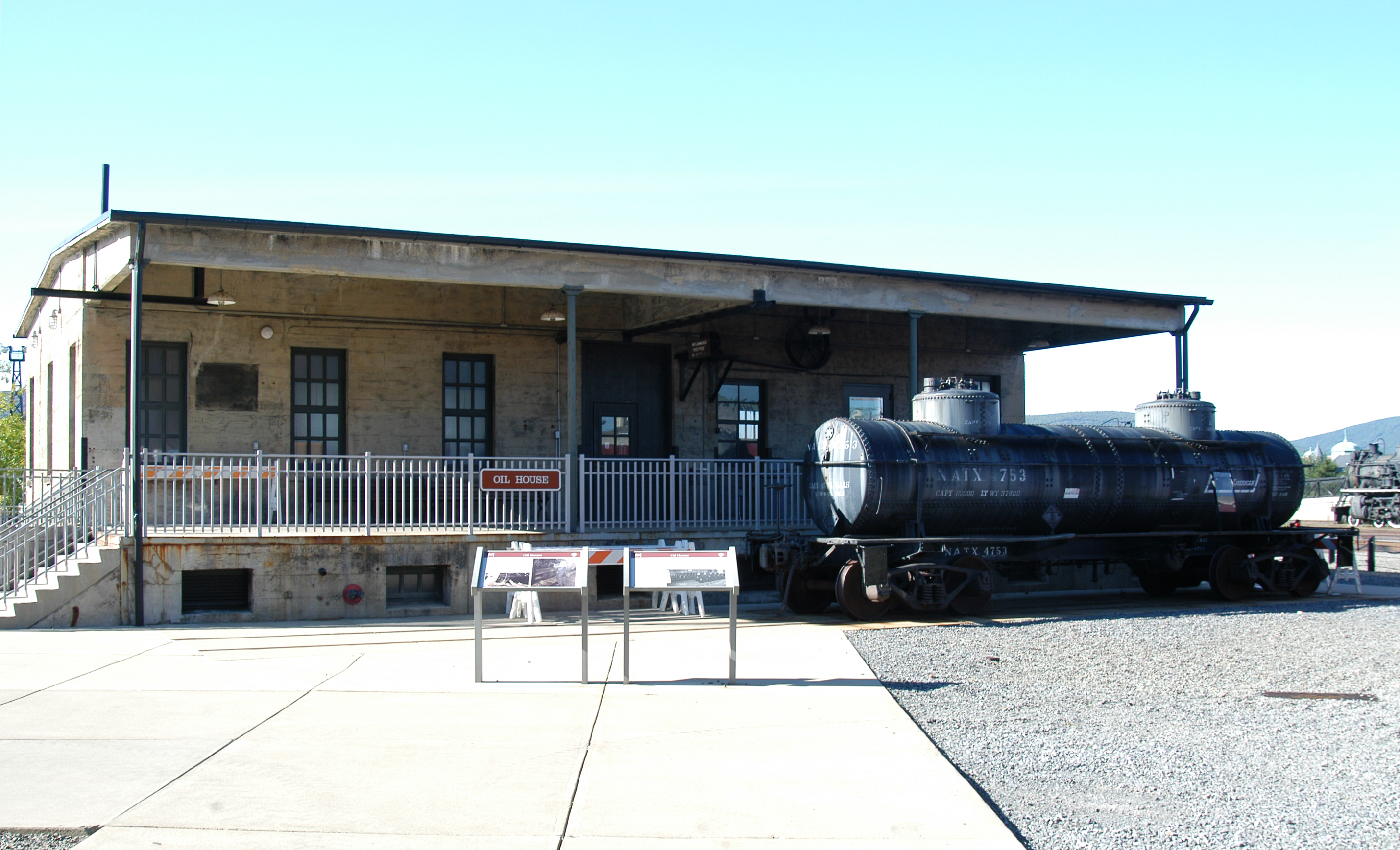Front view of a concrete building with a very large porch and a tank railcar sitting in front of it