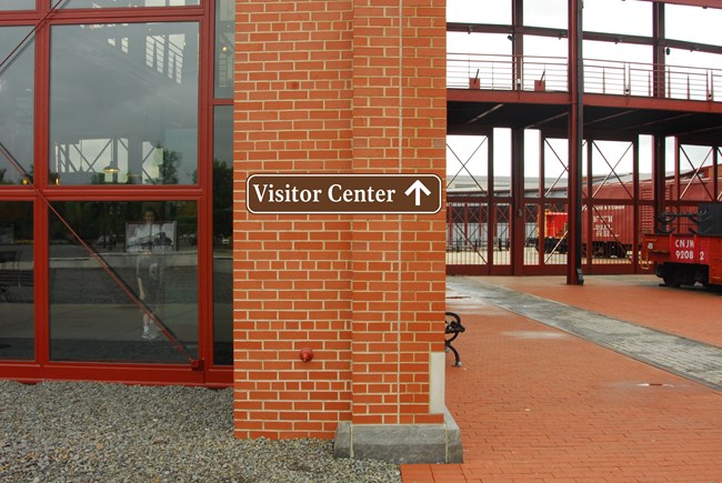 A brown and white sign reading "Visitor Center" attached to a brick wall