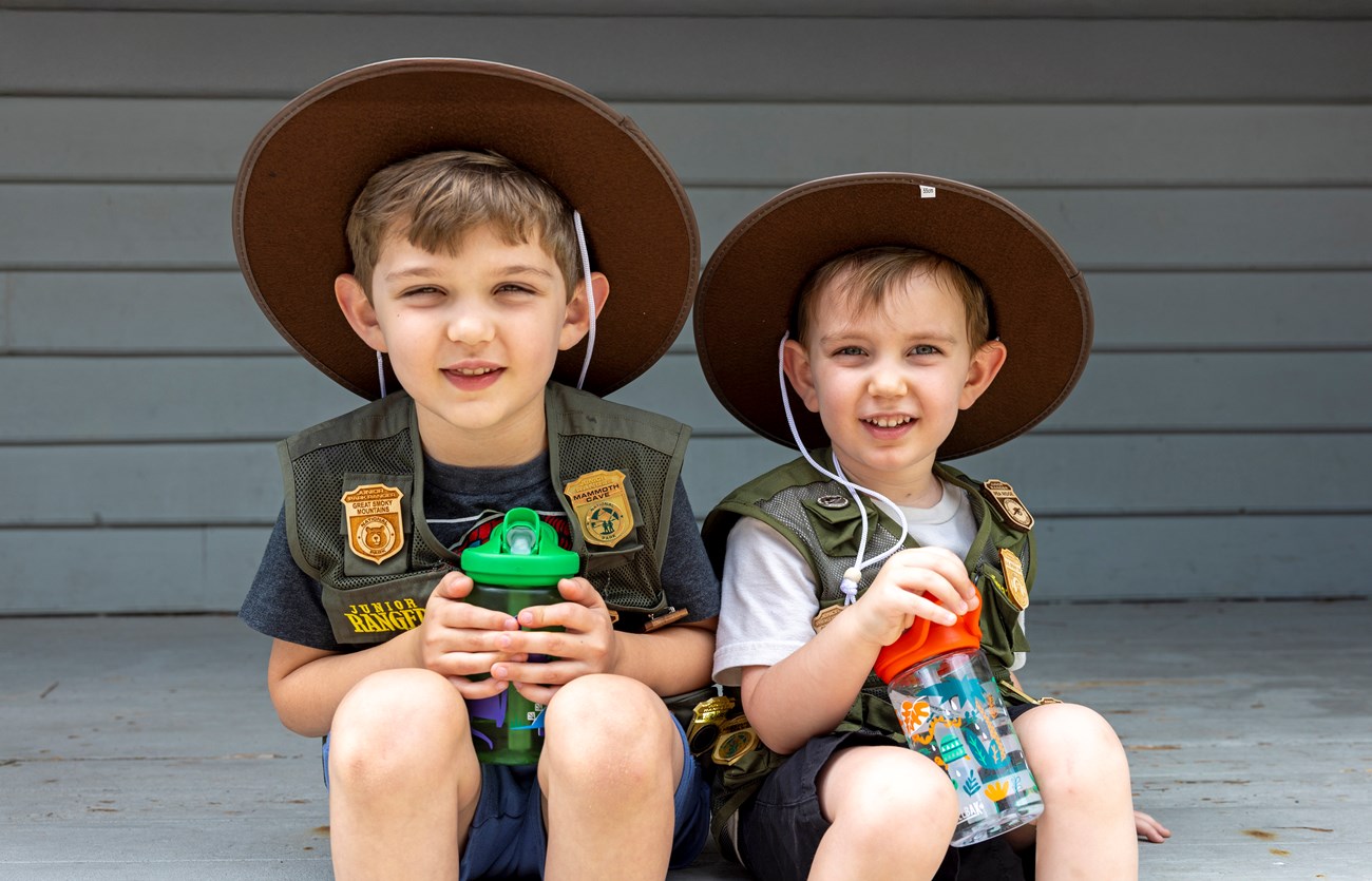 Two boys wearing green junior ranger vests and flat hats