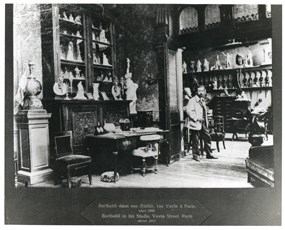 Black and white photo showing a sculptor standing in the midst of an artist studio in 1892.