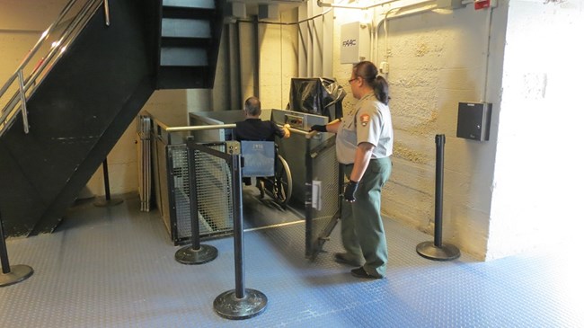 A Park Ranger is opening the door of the wheelchair lift allowing the visitor to exit.