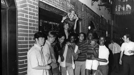 A black and white photo of a group of young people celebrate outside the boarded-up Stonewall Inn.
