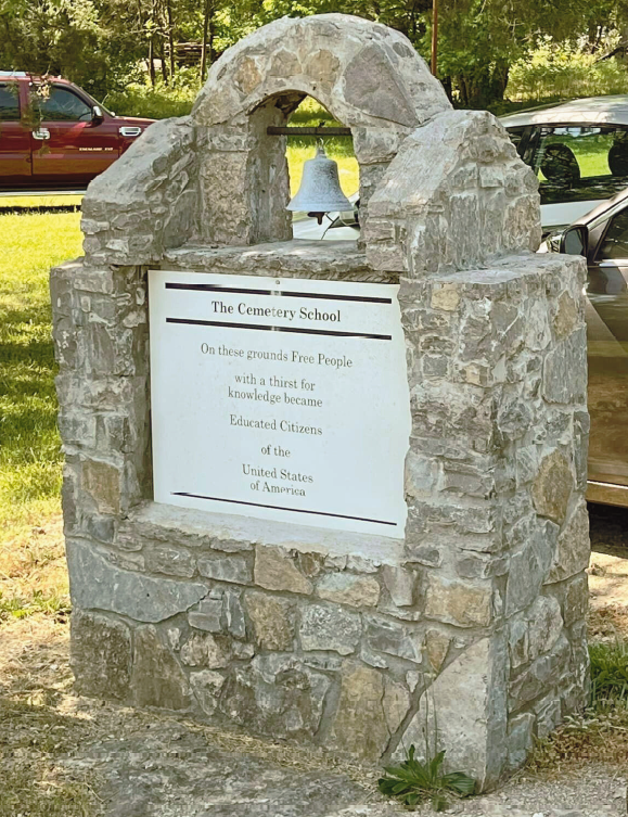 A commemorative plaque framed by stone with a bell at the top.