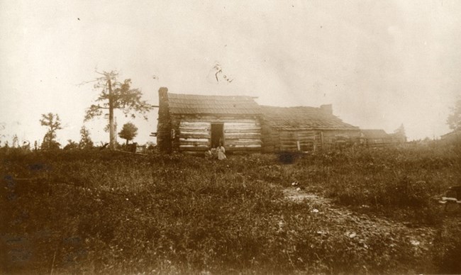 Balck and white photo of a cabin with three Black children standing in front.