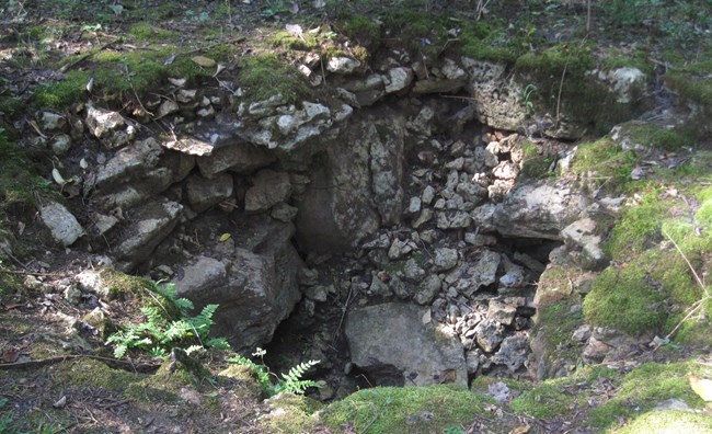 an old well surrounded by collapsing rocks and moss