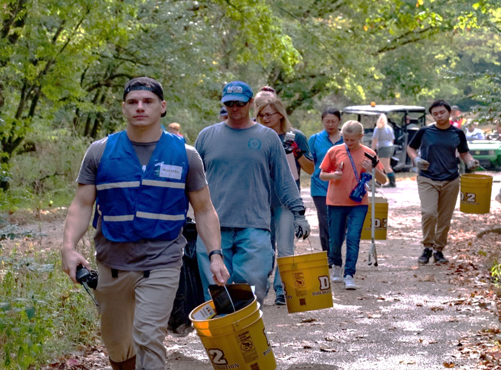 Volunteers walk on trail carrying trash grabbers and buckets.