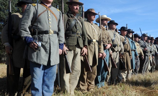 A line of living historians portraying Confederate soldiers holding their muskets.