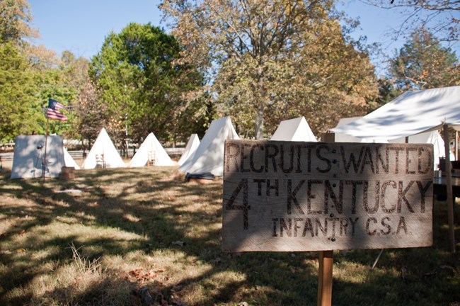 A wooden sign reading "Recruits Wanted 4th Kentucky Infantry, CSA" stands in front of a row of tents.