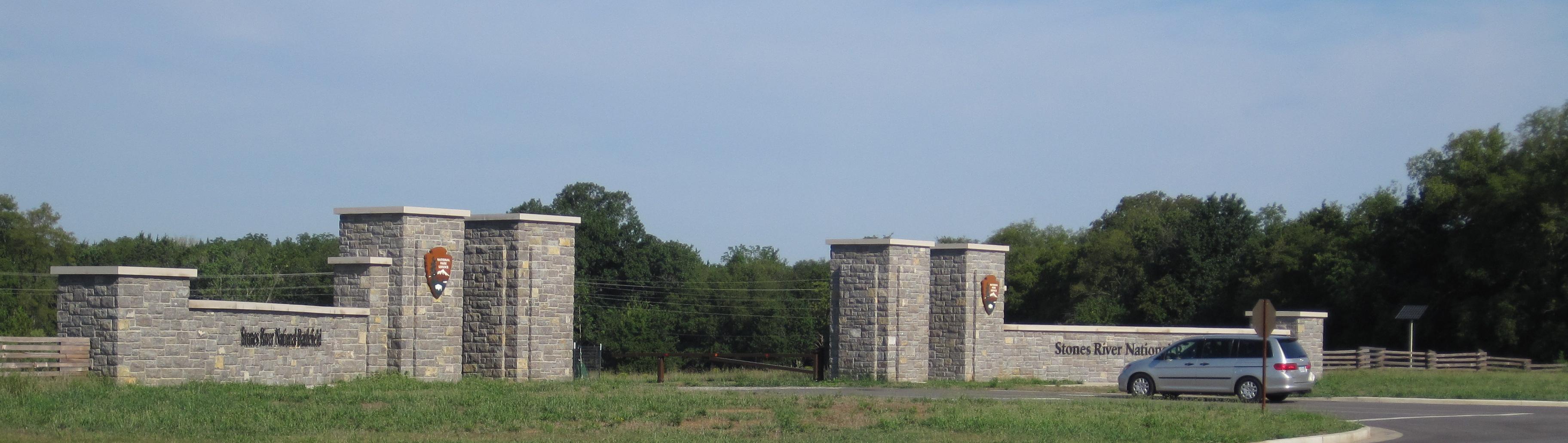 A large stone gateway with a silver van driving through it.
