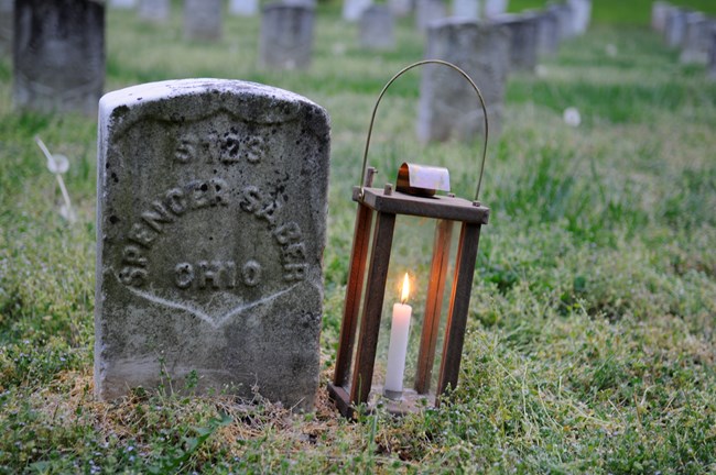 A candle lantern sits next to the national cemetery headstone of Spencer Sober. The stone reads 5723 - Spencer Saber - Ohio.