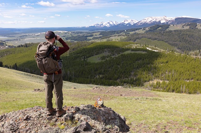 Man in hiking attire looking at distant mountains with binoculars