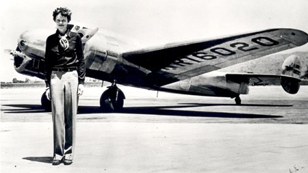 A tall woman stands in front of a plane