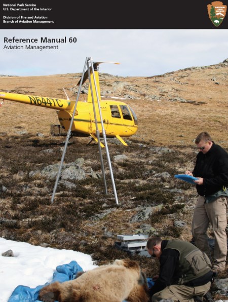 A yellow helicopter on a slope with two men standing over a prone bear