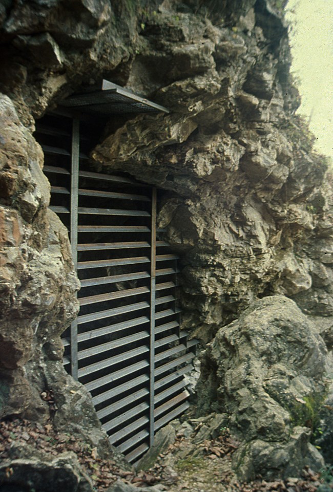 a rocky mine entrance with horizontal metal bars across it