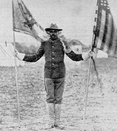 A soldier standing at attention and holding two flags on poles
