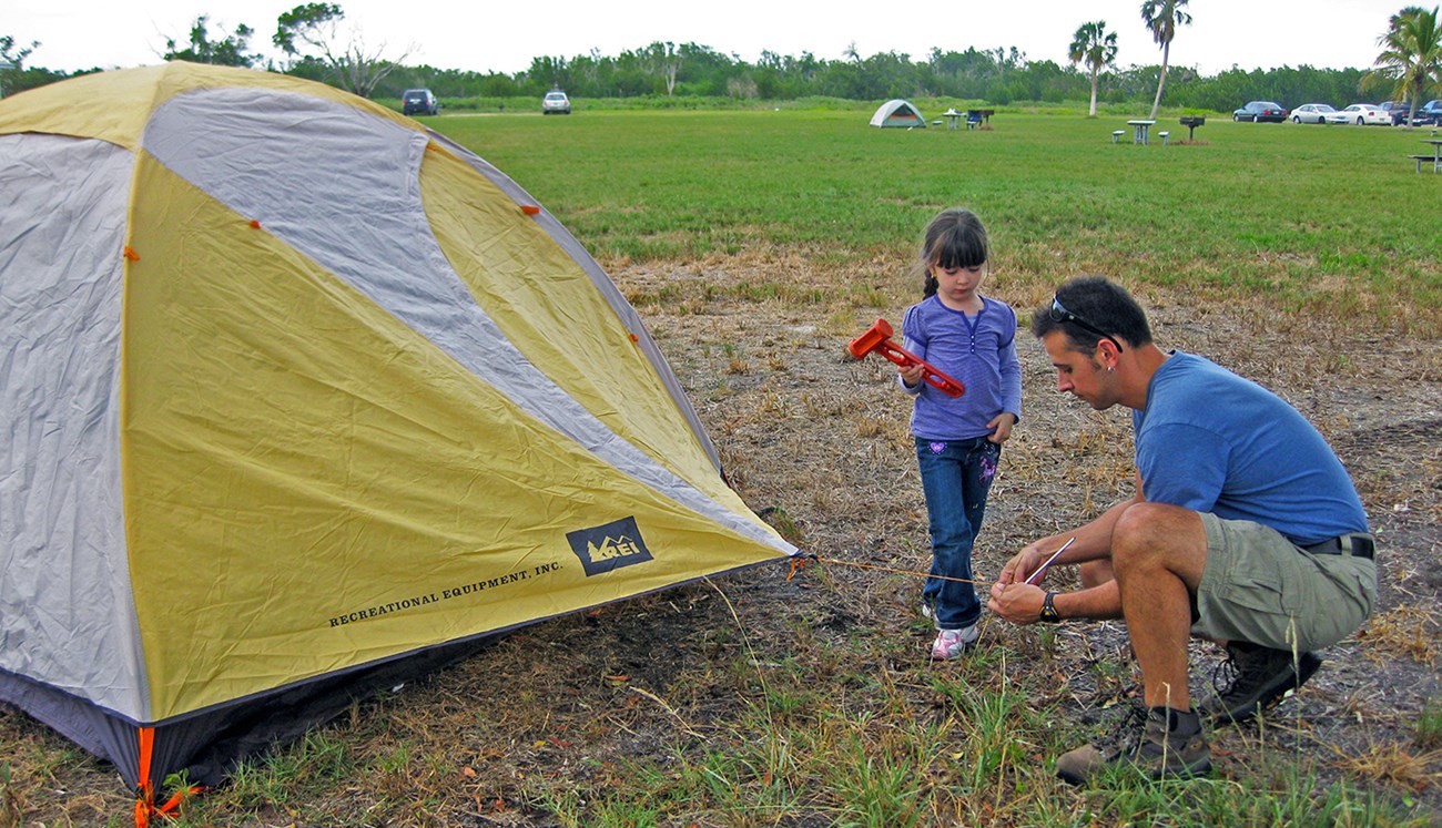 man and young girl set up a yellow tent