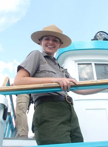 young woman in a ranger uniform smiles and looks down from a platform