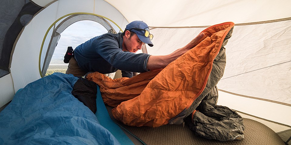 A man unrolls a sleeping bag inside a tent