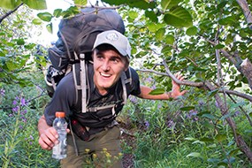 A man walks through thick vegetation carrying a backpack