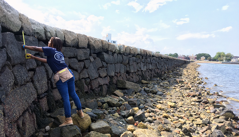 Student intern stands at base of wharf and takes measurements